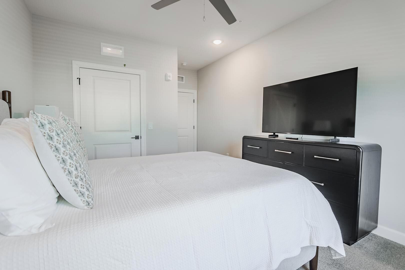 A bedroom with a bed, a TV on a dresser, and a door.