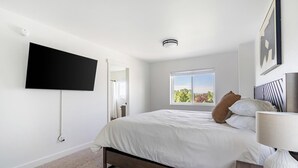 Ein Schlafzimmer mit einem Bett, einem an der Wand befestigten Fernseher, einem Fenster mit Aussicht und einem Nachttisch mit Lampe.