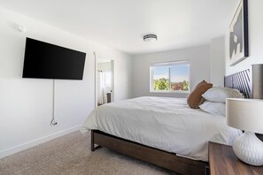A bedroom with a bed, a TV mounted on the wall, a window with a view, and a bedside table with a lamp. - Landing | Modern 3BD, Gym, Clubhouse (Billings)