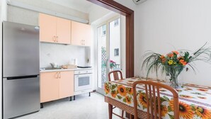 A compact kitchen with a stainless steel refrigerator, peach-colored cabinets, and a dining table with a sunflower tablecloth. - Augusto 42 apartment Napoli.  Stadium Metro & Free Parking (Napoli)
