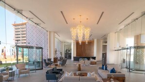Un'ampia hall con arredi moderni, un grande lampadario e ampie finestre che offrono vista su un edificio e palme.