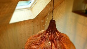 Une pièce avec un plafond en pente, un puits de lumière et un luminaire suspendu de couleur orange, recouvert d’un filet.