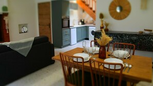Un coin repas avec une table en bois, dressée pour quatre personnes, entourée de chaises. Un vase contenant des plantes séchées est posé sur la table.