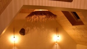 Une chambre mansardée chaleureuse avec un plafond en pente, un lit avec une literie verte, deux lampes de chevet et un banc en bois.