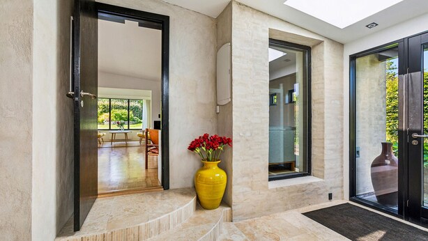 Ein modernes Interieur mit einer gelben Vase voller roter Blumen, einem Essbereich mit Tisch und Stühlen und einem großen Fenster mit Blick auf Grünflächen.
