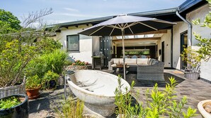 Eine Terrassenanlage im Freien mit einem großen Steinpflanzgefäß, Korbmöbeln und einem Grill.