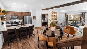 A modern kitchen with a central island, dining area with chairs, and a living room with a sofa and a coffee table.