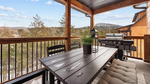 A wooden deck with a table and chairs, a grill, and a potted plant.