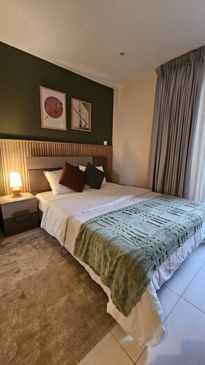 A neatly arranged bedroom with a bed, a nightstand, a lamp, and two framed artworks on the wall. - Peravi Suites at The Bantree (Accra)