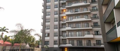 A multi-story residential building with balconies, a well-maintained lawn, and surrounding greenery.