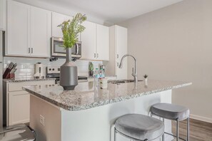 Een moderne keuken met witte kasten, een granieten aanrecht, een roestvrijstalen spoelbak en een barstoel.