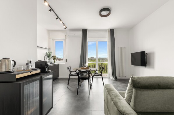 A modern living room with a flat-screen TV, a sofa, a dining area with a table and chairs, and a balcony with a view. - Modern and cozy penthouse for independent living with all amenities. (Milano)