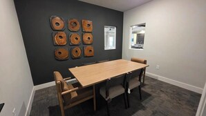 A conference room with a long table, six chairs, and a dark wall with circular wooden art pieces. - Landing | Modern 1BD, Gym, Pool (San Marcos)