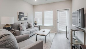 Una sala de estar moderna con un sofá gris, una mesa de centro, un televisor sobre un mueble bajo y una puerta con persianas.