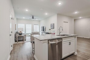 A modern kitchen with a large island, stainless steel appliances, and a dining area with a sofa and table. - Landing | Stunning 2BD, Gym, Clubhouse (San Marcos)