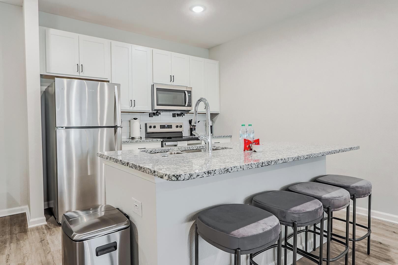 A modern kitchen with white cabinets, stainless steel appliances, a granite countertop, and bar stools.