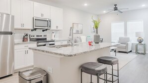Una cocina moderna con armarios blancos, electrodomésticos de acero inoxidable, encimera de granito y una barra con taburetes.