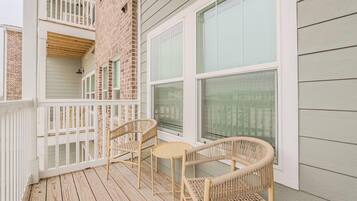 A wooden deck with two wicker chairs and a small table, overlooking a brick building with large windows.
