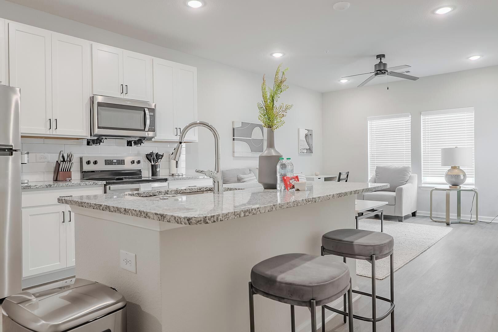 A modern kitchen with white cabinetry, a granite countertop, a built-in microwave, and a stainless steel refrigerator.