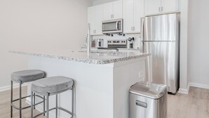 Una cocina moderna con gabinetes blancos, electrodomésticos de acero inoxidable, una encimera de granito y dos taburetes de bar.