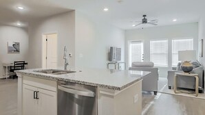 Una cocina moderna con una isla central, electrodomésticos de acero inoxidable y una zona de comedor con un sofá y una pequeña mesa.