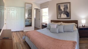 Une chambre à coucher avec un lit, des tables de chevet, un miroir, un tableau et une porte.
