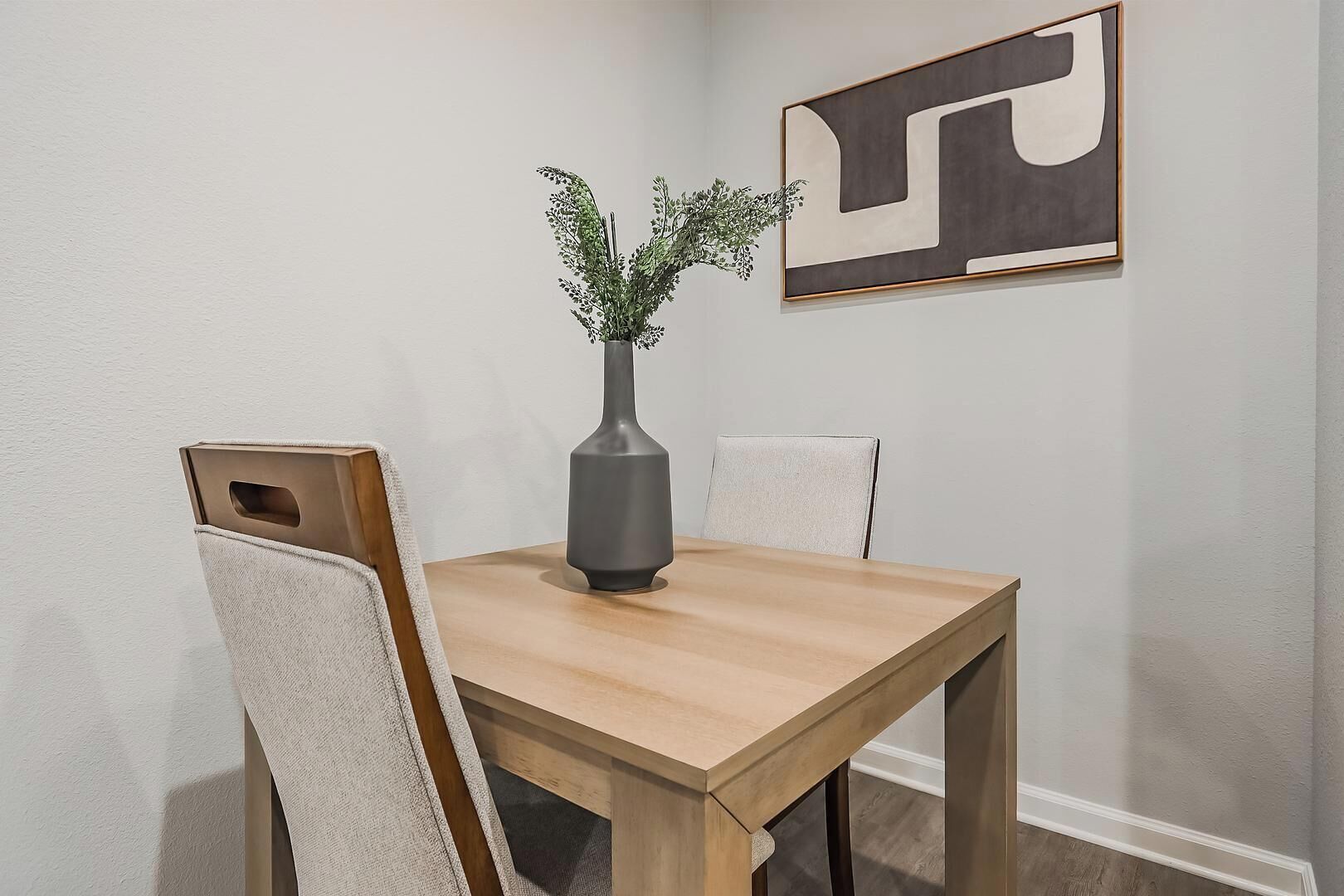 A dining table with a vase of greenery, two chairs, and a large abstract painting on the wall.