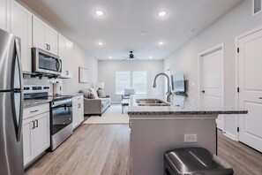 A modern kitchen with stainless steel appliances, a central island, and a dining area with a sofa and table. - Landing | Amazing 1BD, Gym, Clubhouse (San Marcos)