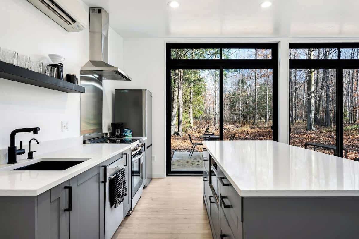 The open-concept living area boasts large floor-to-ceiling windows, flooding the space with natural light and offering picturesque views of the wooded property.