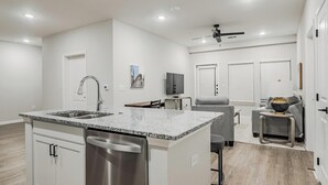 Una cocina moderna con encimeras de granito, electrodomésticos de acero inoxidable y un comedor con sofá gris y una pequeña mesita.