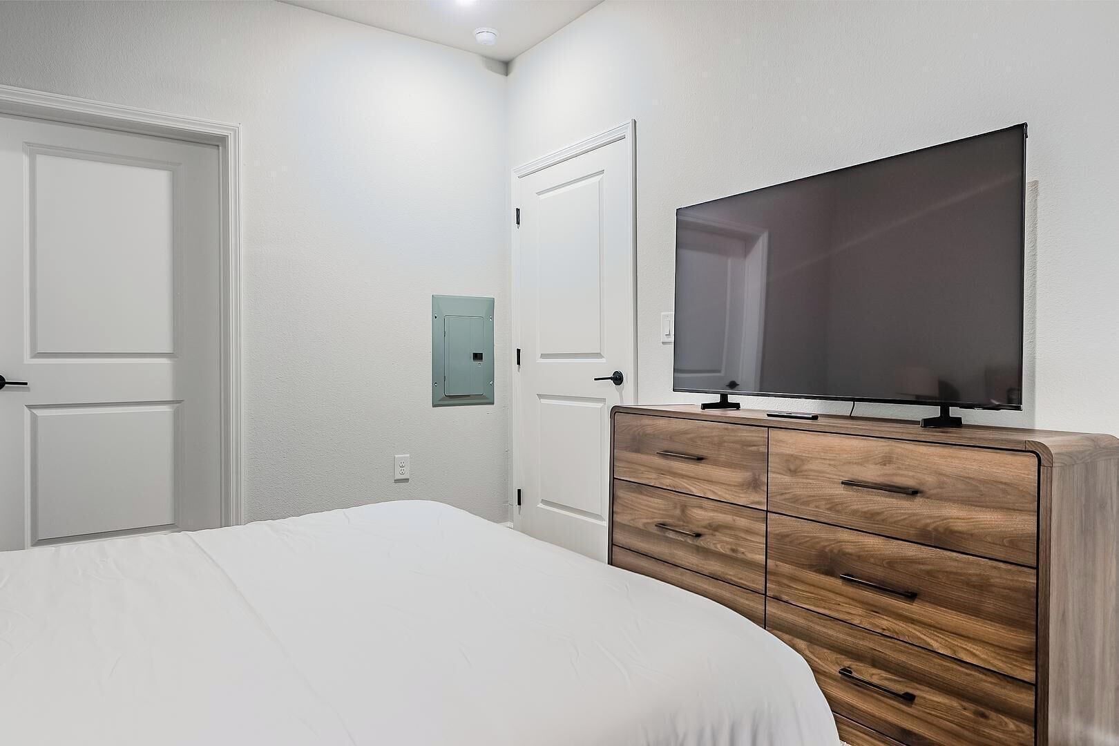 Une chambre à coucher comprenant un lit, une commode en bois, un téléviseur et deux portes.