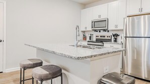 Una cocina moderna con armarios blancos, electrodomésticos de acero inoxidable, encimera de granito y dos taburetes de bar.
