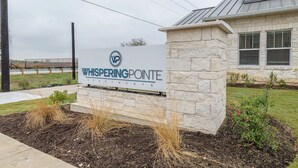 Señal para Whispering Pointe Apartments, con base de piedra y vista despejada del edificio al fondo.