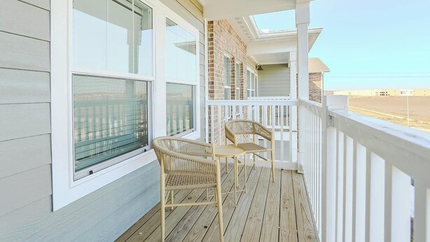 Une terrasse en bois avec deux fauteuils en osier et une table, donnant sur un paysage plat.