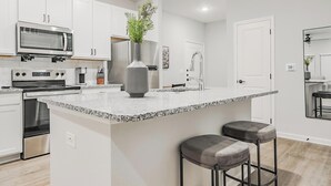 Une cuisine moderne avec des meubles blancs, des appareils en acier inoxydable, un plan de travail en granit et un îlot central doté de tabourets de bar.