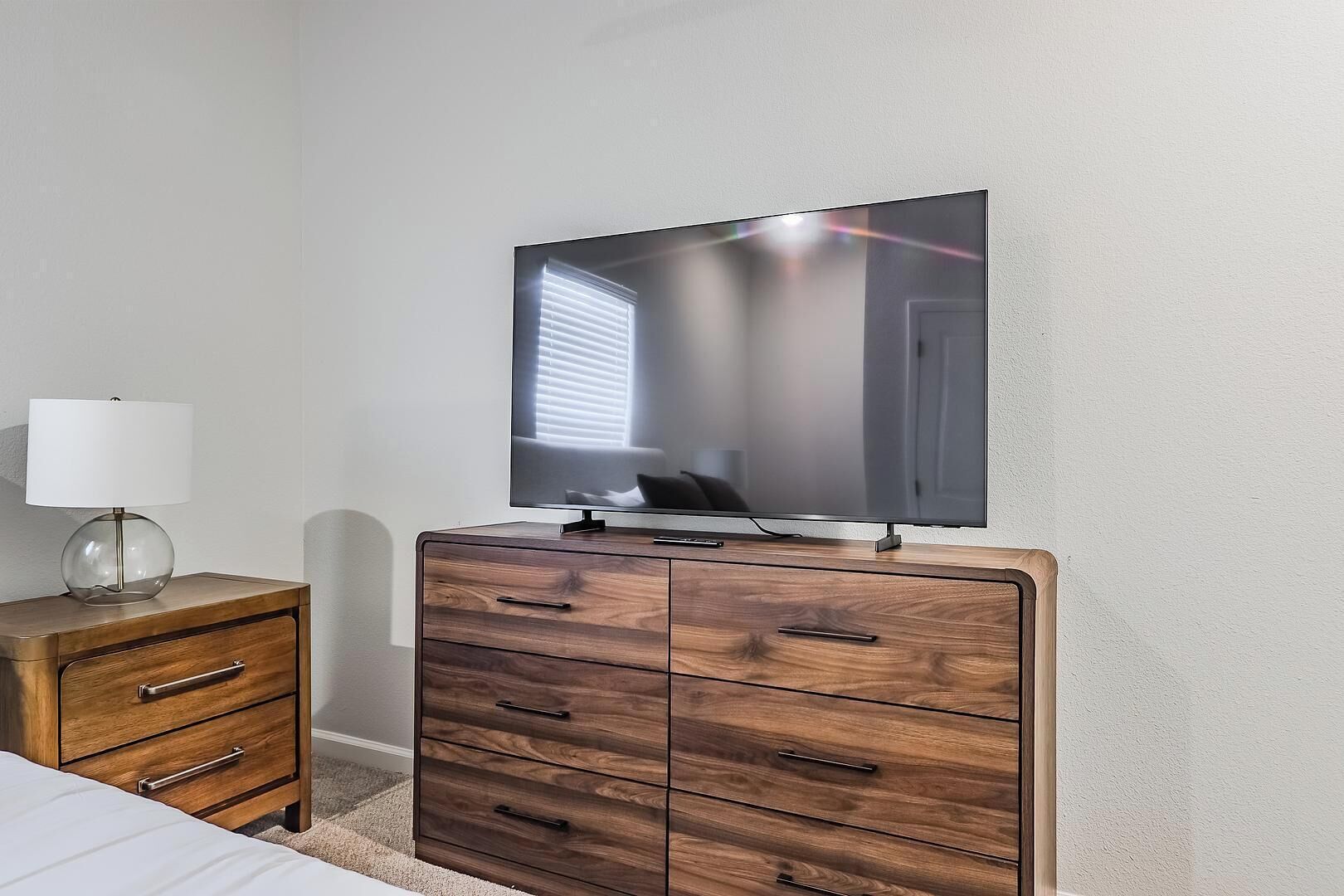 A bedroom with a TV on a dresser, a lamp, and a bed.