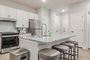 A modern kitchen with white cabinets, stainless steel appliances, a granite countertop, and a bar stool area. - Landing | Spectacular 2BD, Clubhouse, Gym (San Marcos)