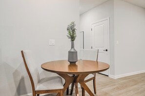 A dining area with a round wooden table, two upholstered chairs, and a grey vase with a plant. - Landing | Spectacular 2BD, Clubhouse, Gym (San Marcos)