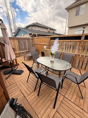 Eine Holzterrasse mit einem runden Glastisch und Stühlen, umgeben von einem Holenzaun.