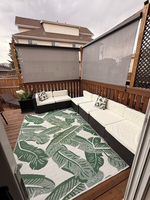 A covered outdoor seating area with a patterned rug, wooden deck, and a view of a house in the background. -     Sylvan Lake Family Retreat | 5-Min Walk to Beach | Sleeps 10 (Sylvan Lake)