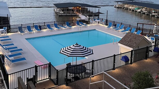 A swimming pool with lounge chairs and a deck area, surrounded by water and a dock. -  3Bed2Bath Waterfront Condo - Alluring Main Channel and Pool Views! (Osage Beach)