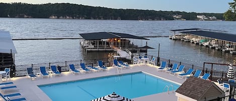 Una piscina con sillas de descanso y una terraza, rodeada de agua y un muelle.