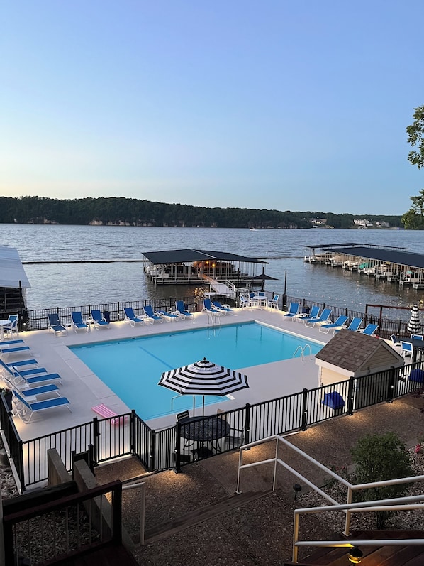 A swimming pool with lounge chairs and a deck area, surrounded by water and a dock. - 3Bed2Bath Waterfront Condo - Alluring Main Channel and Pool Views! (Osage Beach)