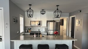 A modern kitchen with white cabinets, a stainless steel refrigerator, a central island with stools, and pendant lighting. -  3Bed2Bath Waterfront Condo - Alluring Main Channel and Pool Views! (Osage Beach)