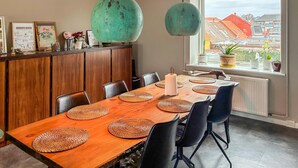 A dining area with a wooden table, black chairs, woven placemats, and a view of buildings through a large window. - 3 bedroom lovely apartment in Korsør (Korsør)