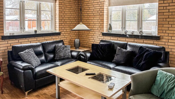 A living room with a brick wall, two black leather sofas, a glass coffee table, and a lamp. - Lovely home in Eskebjerg with WiFi (Eskebjerg)