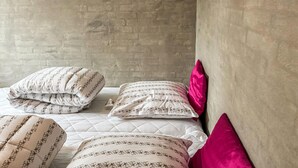 A bed with striped pillows and a quilted cover in a room with a brick wall and a plain wall. - Lovely home in Eskebjerg with WiFi (Eskebjerg)