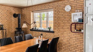 A dining area with a brick wall, a wooden table, black chairs, a black stove, a window with a view, and a clock. - Lovely home in Eskebjerg with WiFi (Eskebjerg)