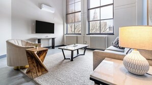 A modern living room with a sofa, armchair, coffee table, and a TV mounted on the wall. - Landing | Stunning 1BD in Downtown Hartford (Hartford)