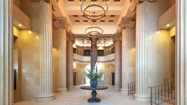 A grand lobby with high ceilings, classical columns, a central chandelier, and a round table with a potted plant. - Landing | Stunning 1BD in Downtown Hartford (Hartford)